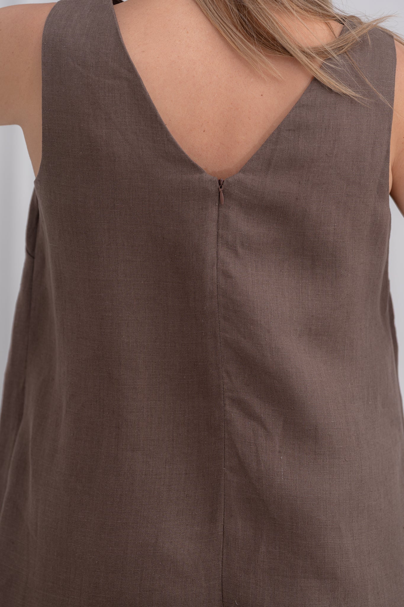 Ilga lininė suknelė su kišenėmis ir skeltuku. Be rankovių. Tamsiai ruda. Nuotraukoje užtrauktuko nugaroje vaizdas iš arti