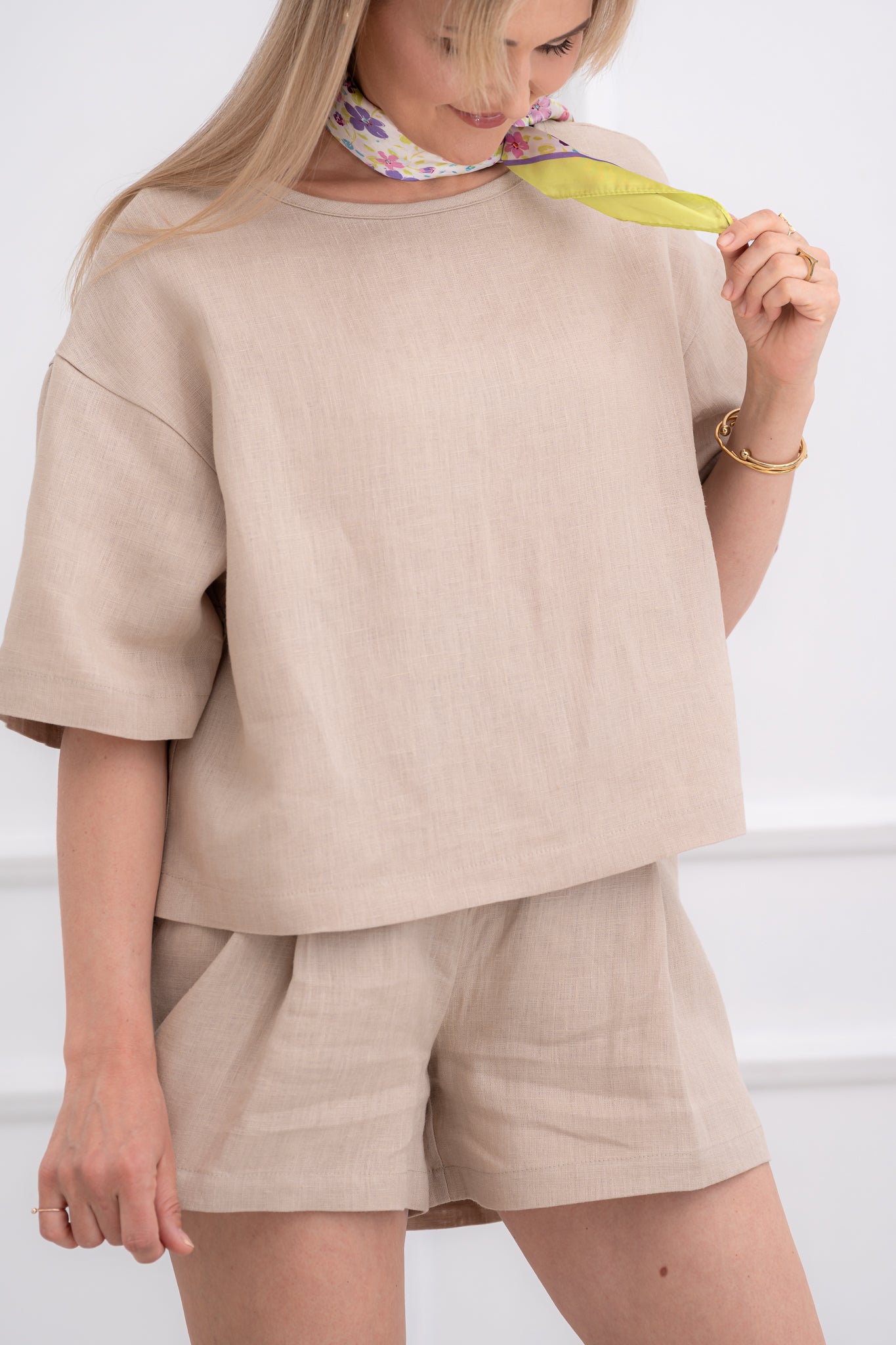 lininiai šortai moterims, trumpi, platūs, su klostėmis priekyje. Liemuo su guma ir raištuku, šortai su kišenėmis. Spalva - smėlio. Modleis apsivilkusi ir derančią lininę palaidinę.