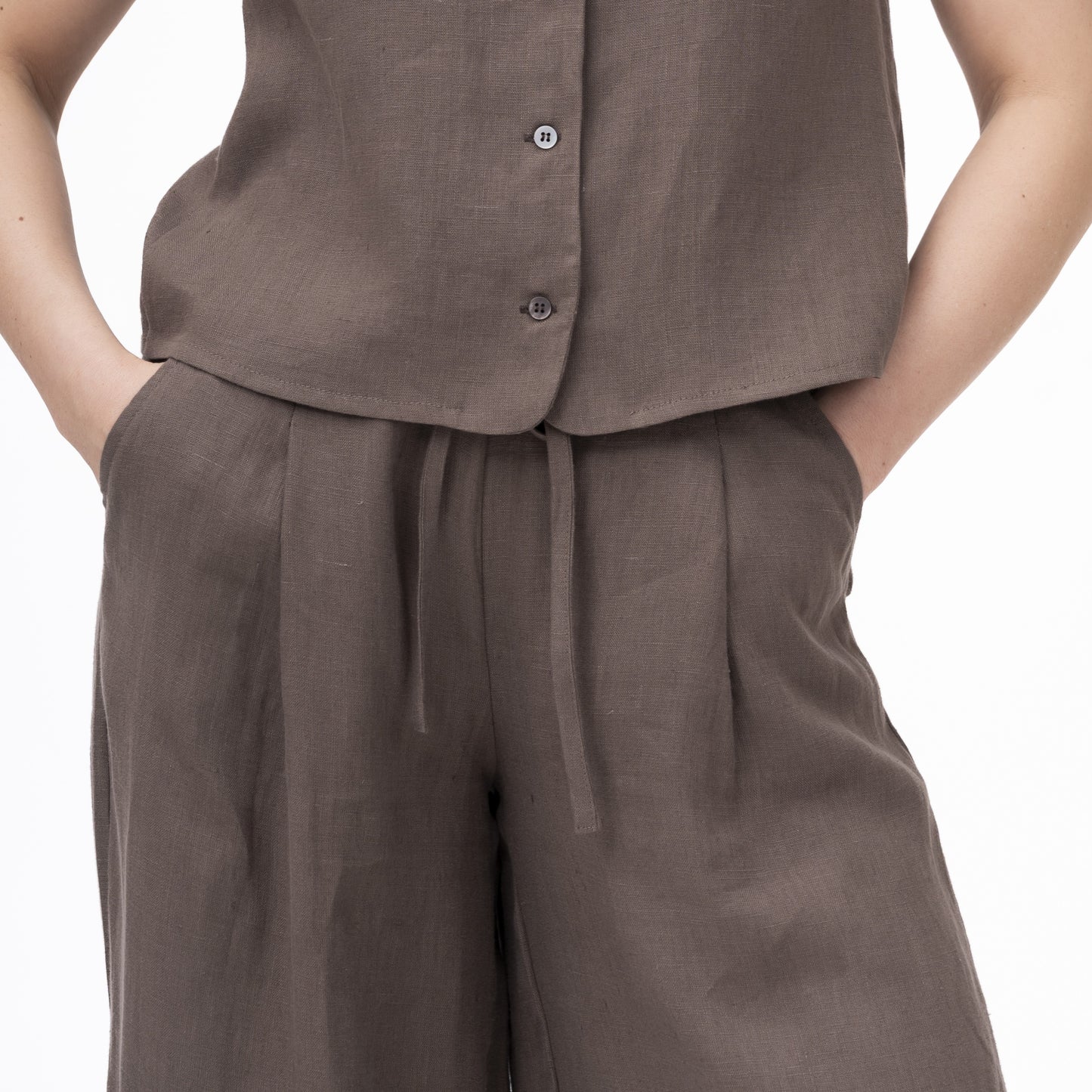 lininės kelnės moterims, tamsiai rudos su kišenėmis ir raišteliais. Priartintas vaizdas iš priekio