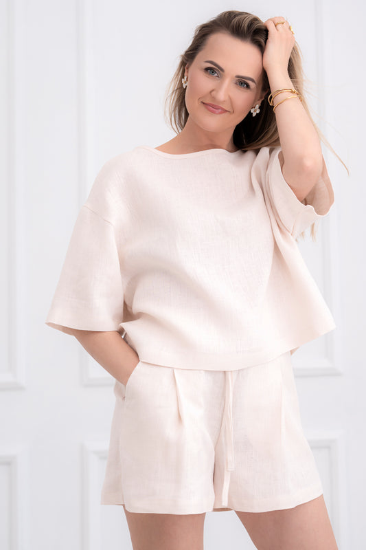 lininiai šortai moterims, trumpi, platūs, su klostėmis priekyje. Liemuo su guma ir raištuku, šortai su kišenėmis. Spalva - kreminė balta. Modelis apsivilkusi ir derančią lininę palaidinę.