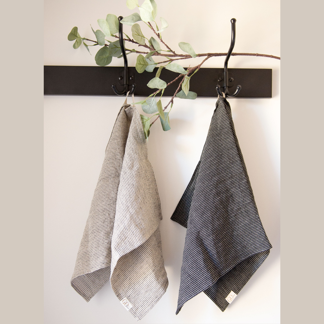 du lininiai virtuvės rankšluostukai, pakabinti ant kabyklos. Viena pilkai dryžuotas, kitas juodai dryžuotas