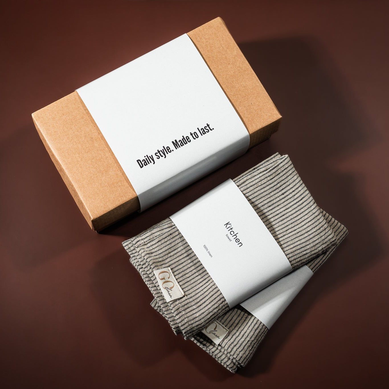lininiai virtuvės rankšluostukai, pilkai dryžuoti, šalia padėta įpakavimo dėžutė