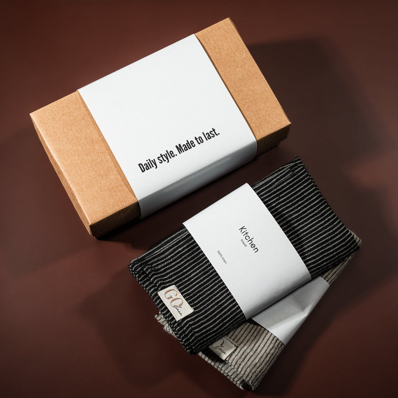 lininiai virtuvės rankšluostukai, 1 juodai dryžuotas kitas pilai dryžuotas , šalia padėta įpakavimo dėžutė