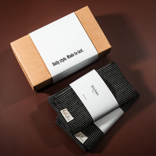 lininiai virtuvės rankšluostukai, juodai dryžuoti, šalia padėta įpakavimo dėžutė