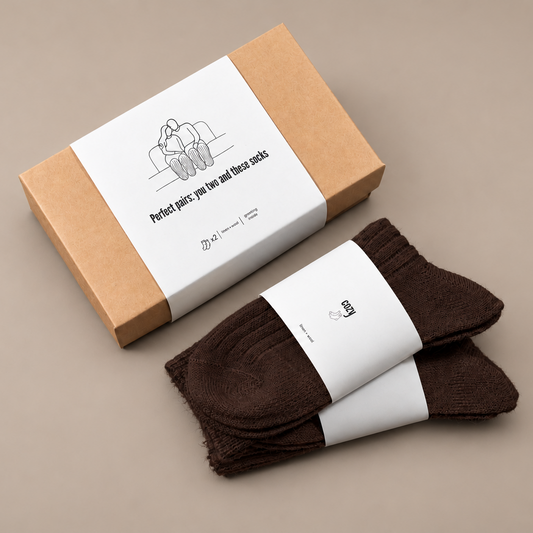 Dvi poros tamsiai rudų lino ir vilnos kojinių šalia dovanų dėžutės su užrašu „Perfect pairs: you two and these socks“.