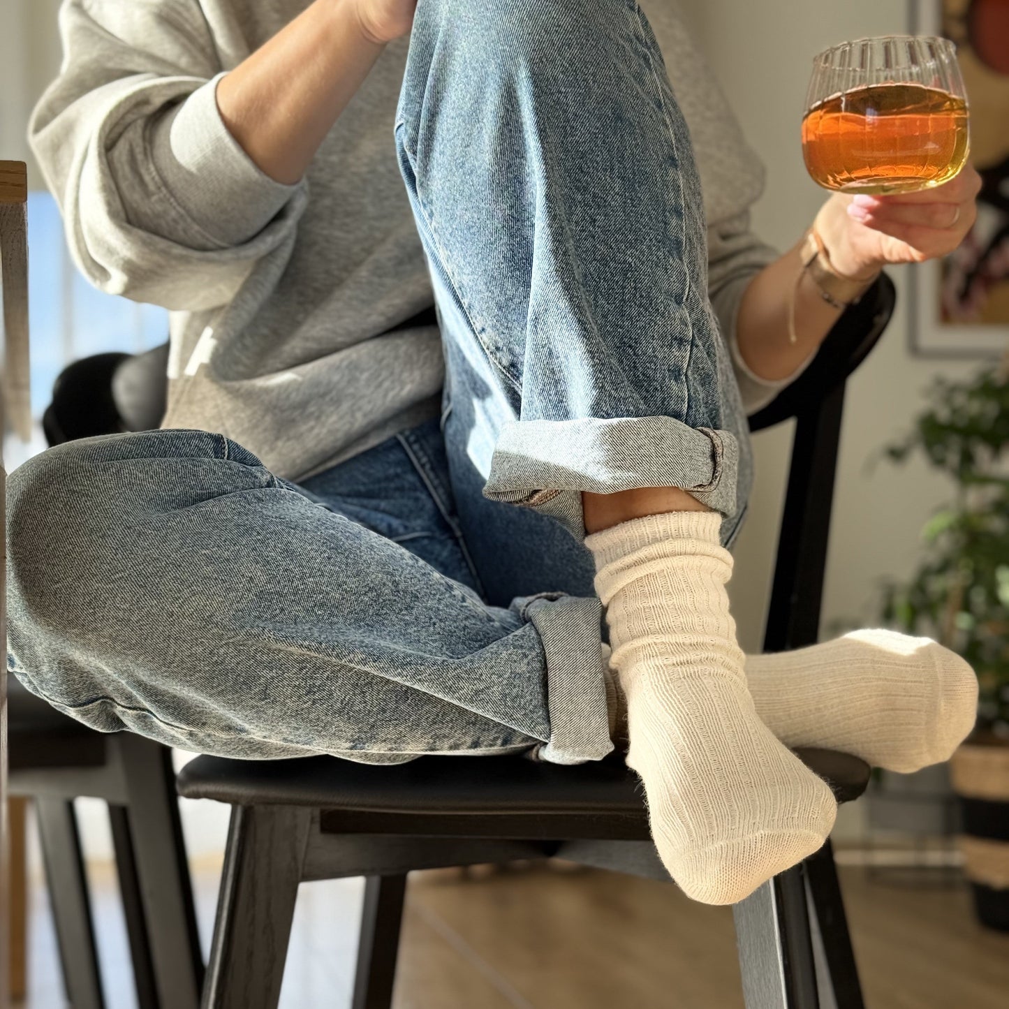 moteris apsimovusi vilnones kojines, sėdi ant kėdės, geria arbatą