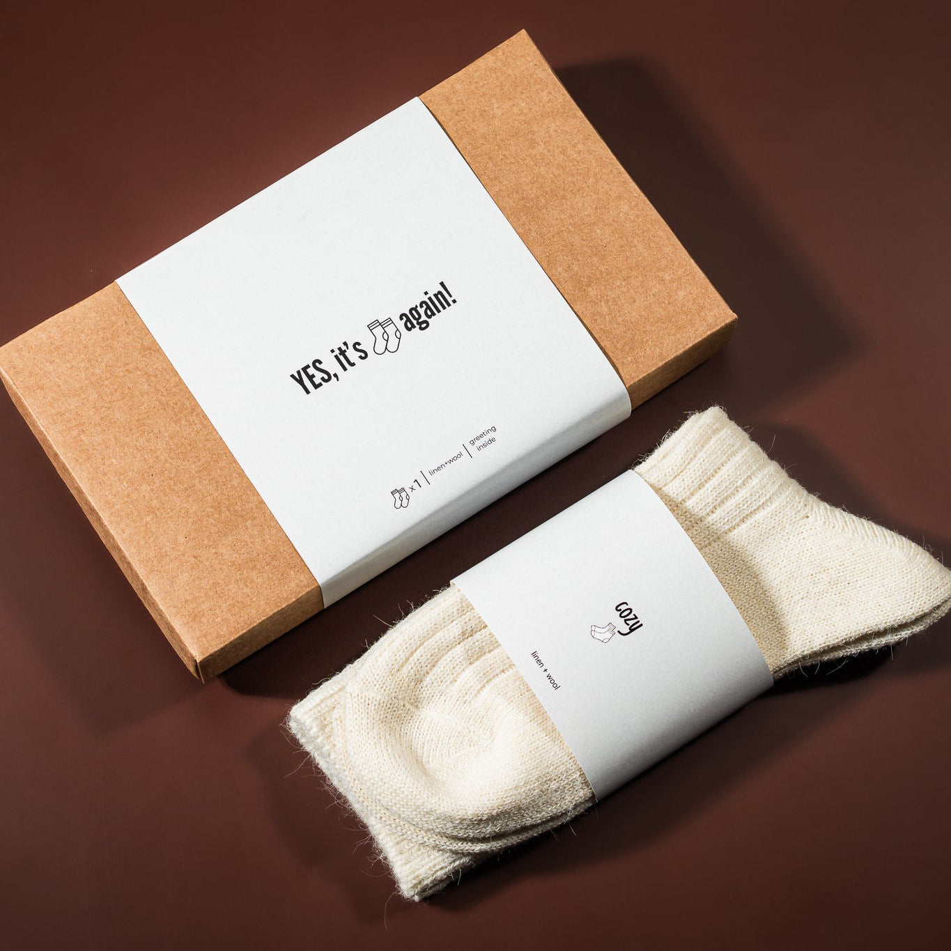 kalėdinė dovana: lino-vilnos kojinės, šalia padėta įpakavimo dėžutė 