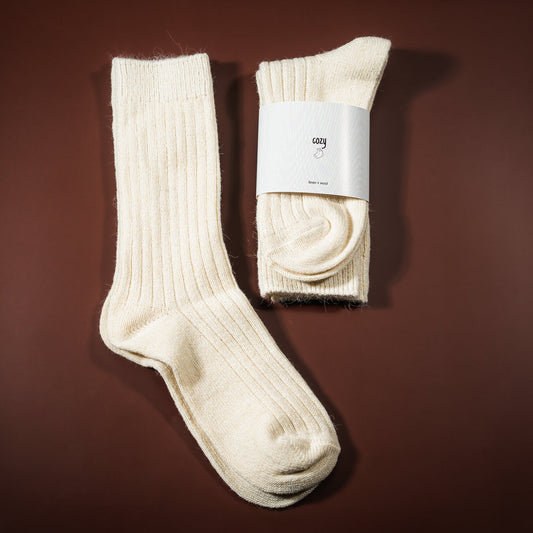 Lino-vilnos kojinė, kreminės baltos spalvos, su etikete cozy socks, ir šalia padėtos kojinės ištiestos be etiketės