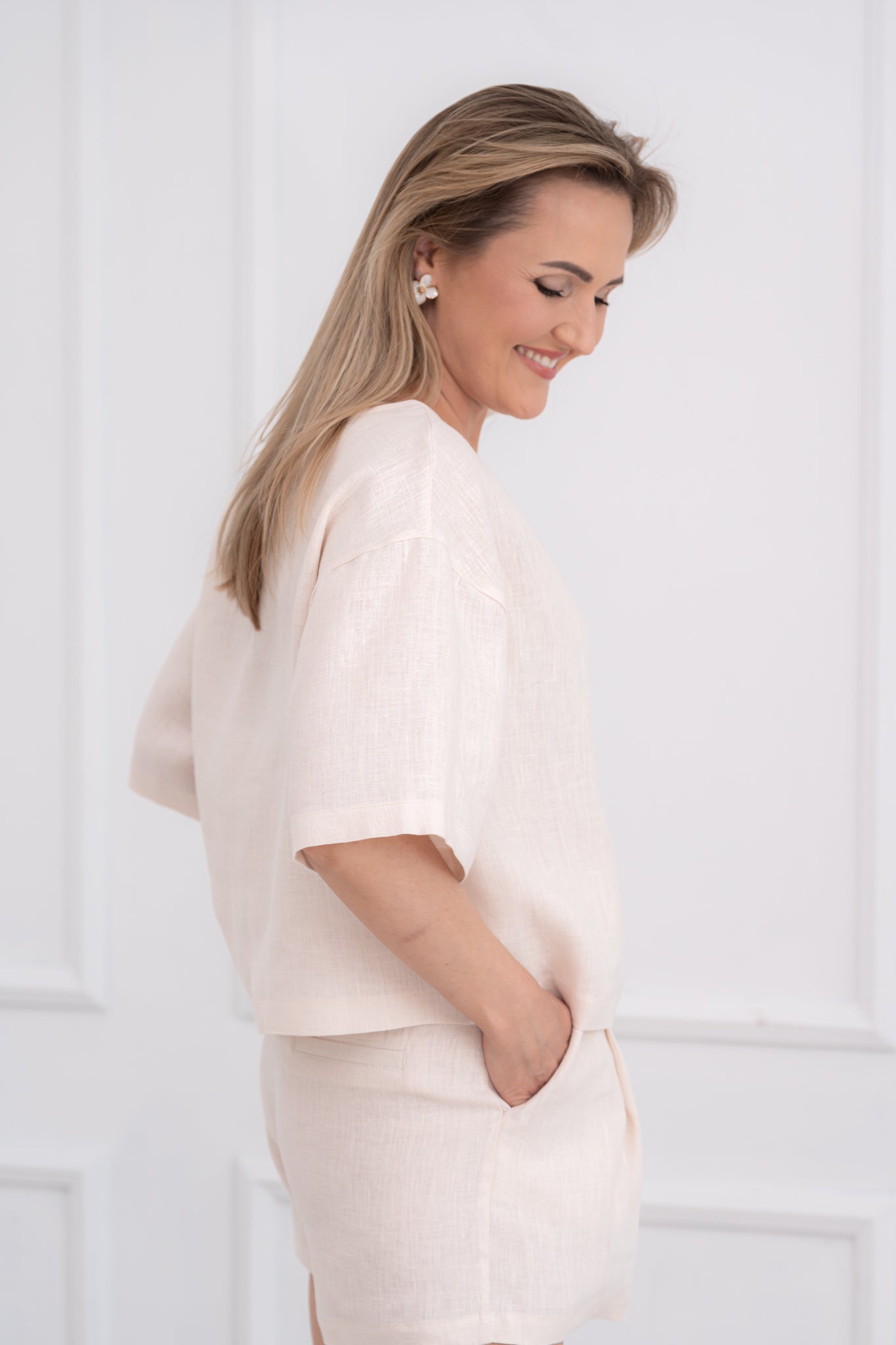 Lininė moteriška palaidinė, didinta, plati, trumpomis rankovėmis. Trumpa, laisvo modelio. Spalva - kreminė balta. Modelis taip pat vilki derančius lininius šortus.