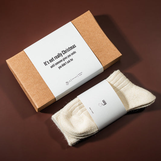 kalėdinė dovana: lino-vilnos kojinės, šalia padėta įpakavimo dėžutė 