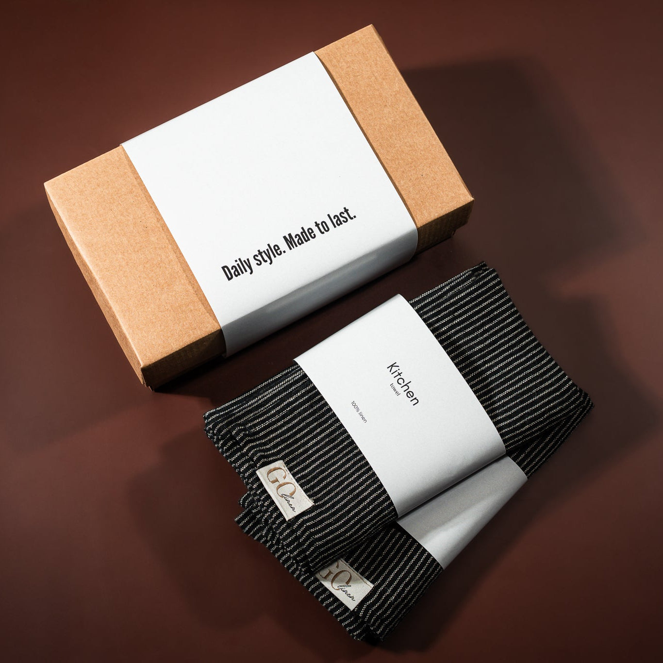 lininiai virtuvės rankšluostukai, juodai dryžuoti, šalia padėta įpakavimo dėžutė