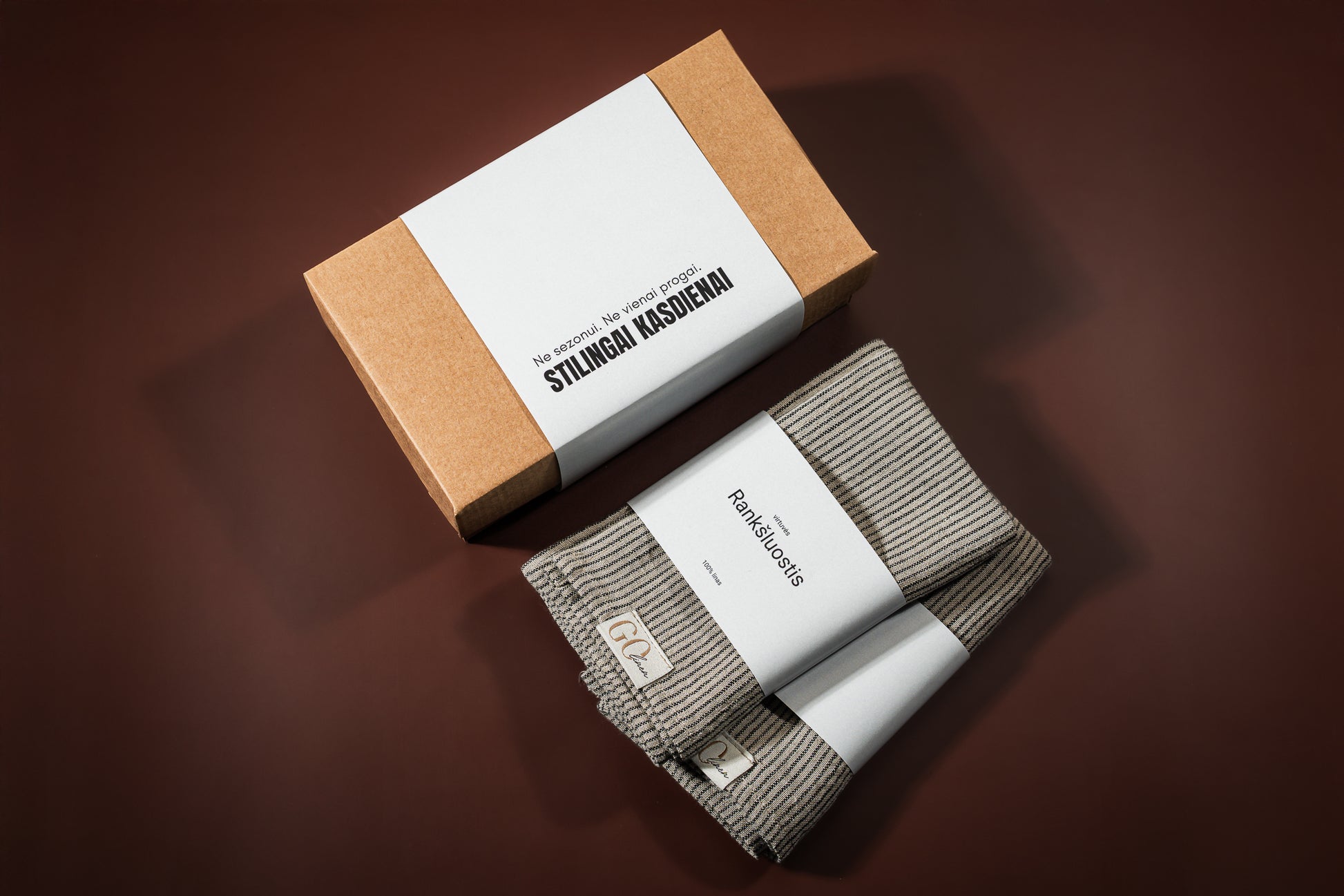 du lininiai virtuvės rankšluostukai, pilkai dryžuoti. Šalia padėta įpakavimo dėžutė